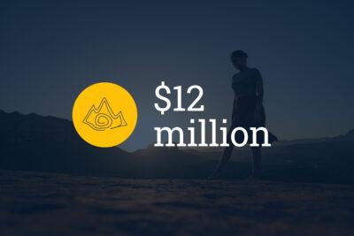 Native woman standing in nature with a sunset behind her. The words "$12 million" and a yellow icon of a mountain on top of photo.